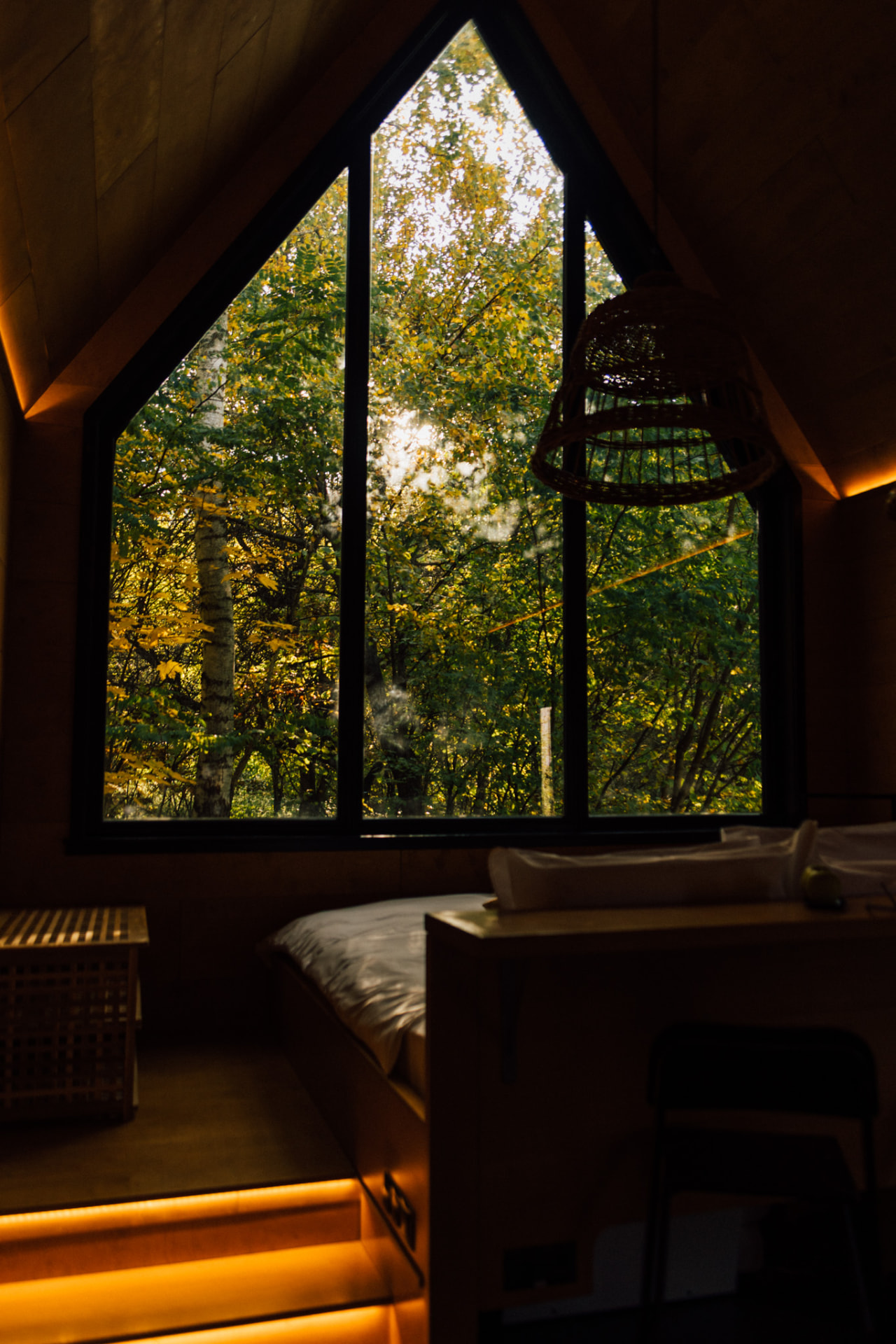 Interior cozy cu fereastra triunghiulară și pădurea de toamnă în fundal
